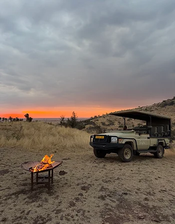A safari vehicle beside a fire on the plains at sunset.